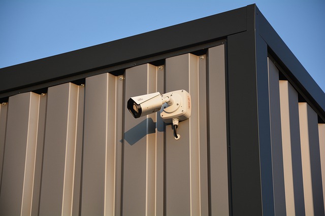 A security camera on the outside wall of a warehouse.
